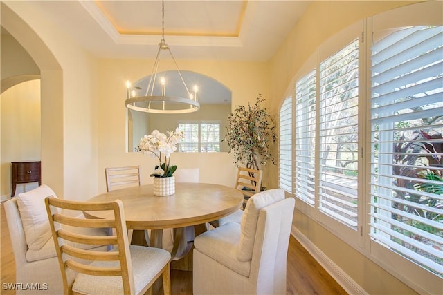 dining room with a tray ceiling, wood-type flooring, and an inviting chandelier