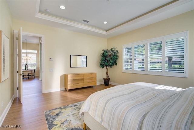 bedroom featuring a raised ceiling, light wood-type flooring, ornamental molding, and a chandelier