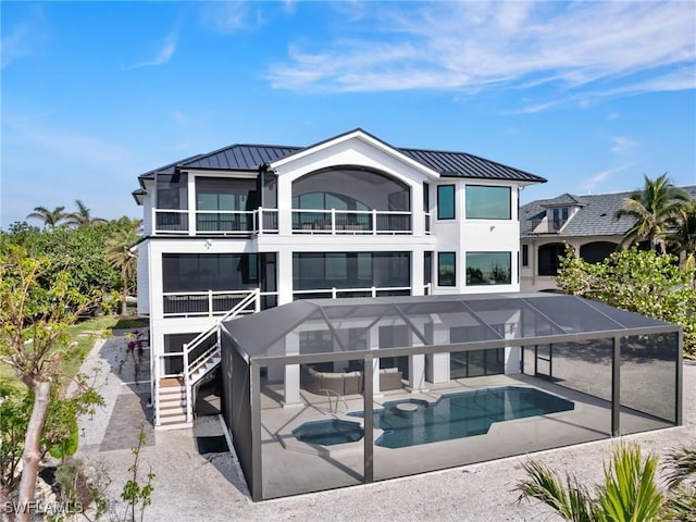 rear view of property featuring glass enclosure, a swimming pool with hot tub, a balcony, and a patio