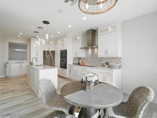 kitchen with white cabinetry, a kitchen island with sink, black appliances, and wall chimney range hood