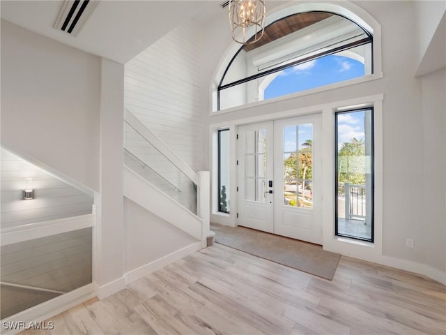 foyer entrance with light hardwood / wood-style floors, a towering ceiling, french doors, and an inviting chandelier