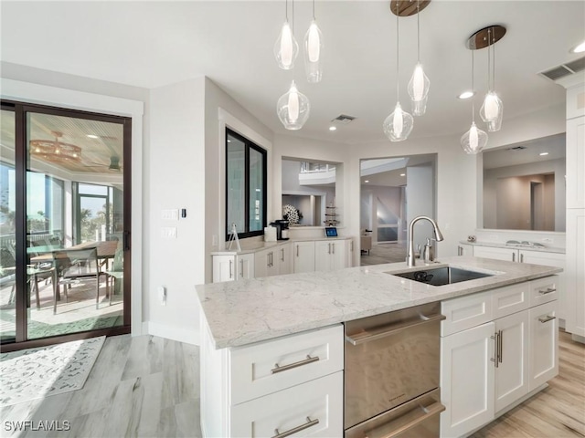 kitchen featuring stainless steel dishwasher, sink, pendant lighting, white cabinetry, and an island with sink