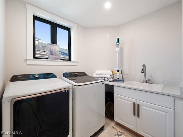 laundry room with washer and clothes dryer, sink, cabinets, and light hardwood / wood-style flooring