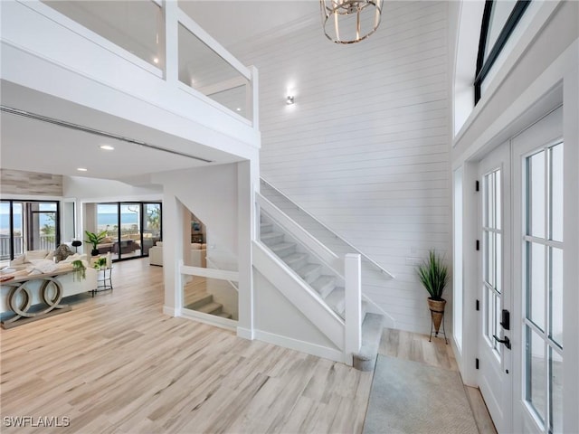 foyer entrance featuring light wood-type flooring, french doors, a towering ceiling, and a notable chandelier