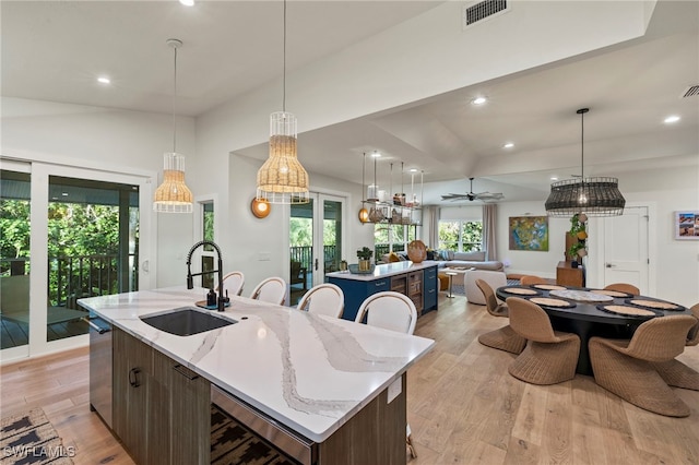 kitchen with light wood-style flooring, a sink, visible vents, open floor plan, and a center island with sink