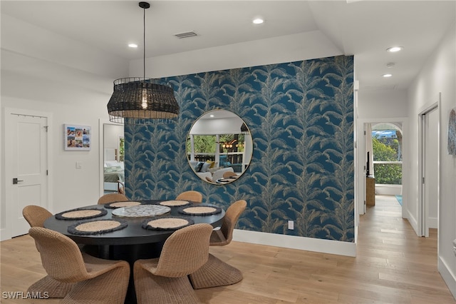 dining space with wallpapered walls, an accent wall, visible vents, and wood finished floors