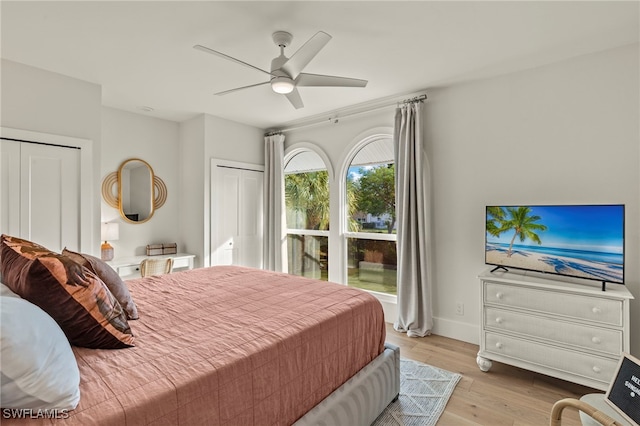 bedroom featuring wood finished floors, two closets, a ceiling fan, and baseboards