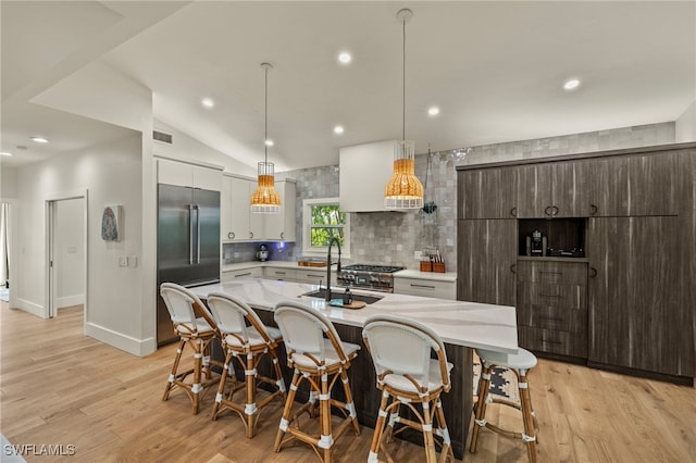 kitchen featuring a sink, high quality appliances, light countertops, tasteful backsplash, and an island with sink