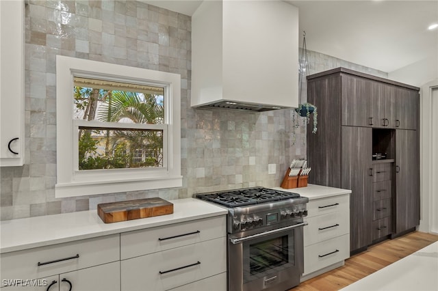 kitchen with premium range hood, light countertops, high end stainless steel range oven, decorative backsplash, and light wood finished floors