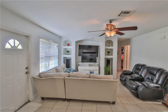 living room with built in shelves, ceiling fan, a fireplace, and light tile patterned flooring