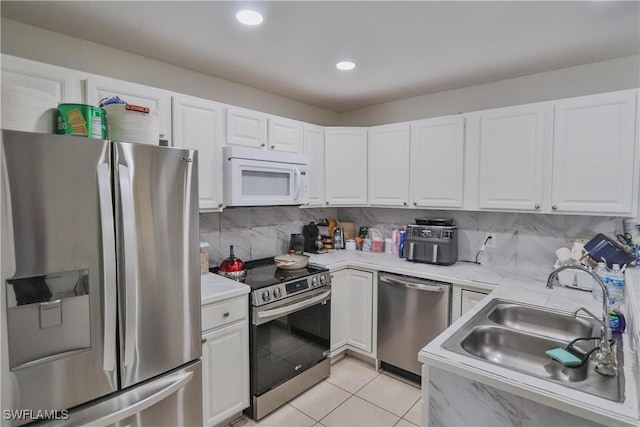 kitchen featuring white cabinetry, sink, decorative backsplash, light tile patterned floors, and appliances with stainless steel finishes