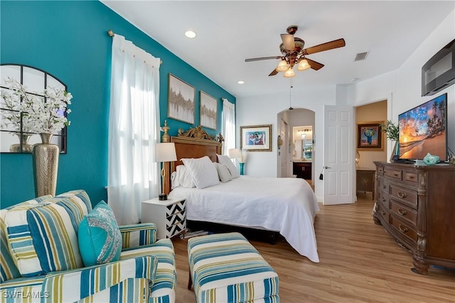 bedroom with ceiling fan, multiple windows, connected bathroom, and light hardwood / wood-style flooring