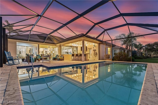 pool at dusk with a lanai, a patio area, and exterior bar