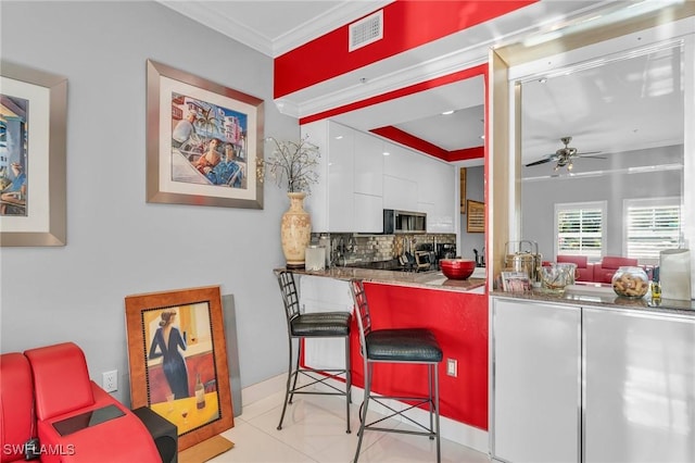 kitchen with a breakfast bar, backsplash, white cabinets, crown molding, and ceiling fan