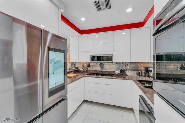 kitchen with white cabinets, decorative backsplash, dark stone countertops, light tile patterned floors, and appliances with stainless steel finishes