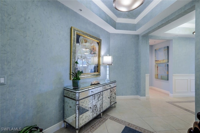 corridor featuring a raised ceiling, light tile patterned floors, and crown molding