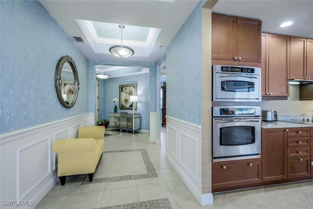 kitchen with light stone counters, light tile patterned floors, a raised ceiling, and stainless steel double oven