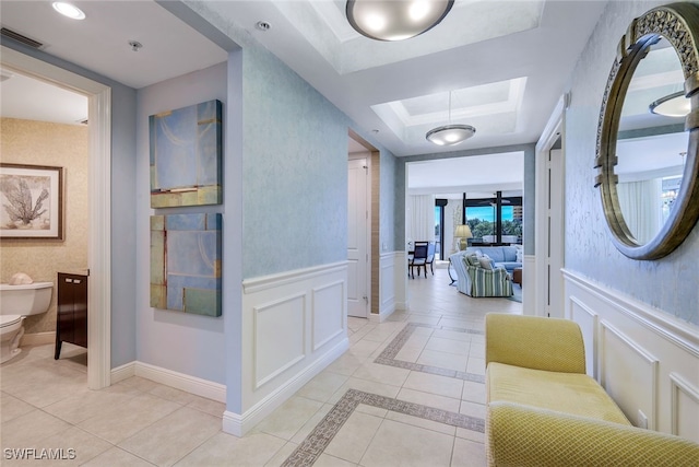 corridor with light tile patterned floors and a tray ceiling