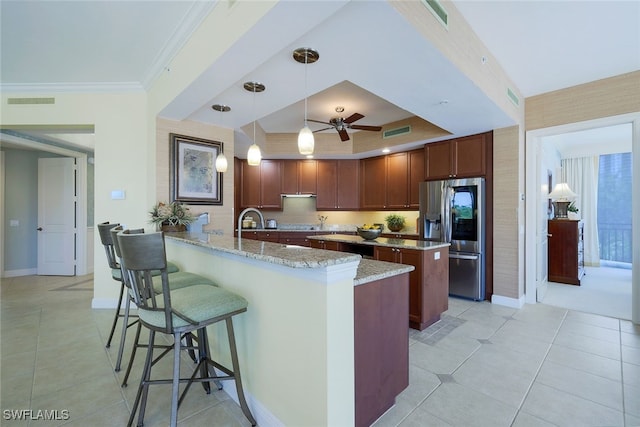 kitchen featuring hanging light fixtures, ceiling fan, a raised ceiling, stainless steel refrigerator with ice dispenser, and light stone countertops