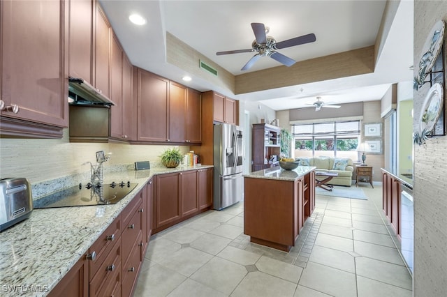 kitchen featuring stainless steel refrigerator with ice dispenser, light stone counters, a tray ceiling, a kitchen island, and black electric stovetop