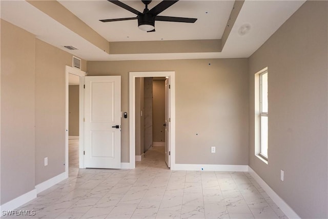 empty room with ceiling fan and a tray ceiling