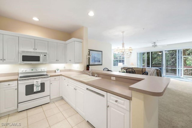 kitchen featuring a chandelier, a peninsula, white appliances, white cabinetry, and a sink