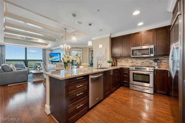 kitchen featuring stainless steel appliances, ornamental molding, open floor plan, dark wood-type flooring, and a peninsula