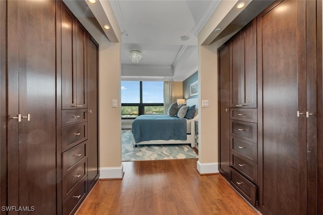hallway featuring baseboards, crown molding, wood finished floors, recessed lighting, and a tray ceiling