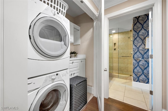 laundry room featuring stacked washer and dryer, baseboards, ornamental molding, and dark tile patterned flooring