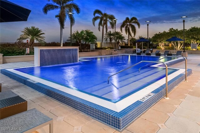 pool at dusk featuring a patio and pool water feature