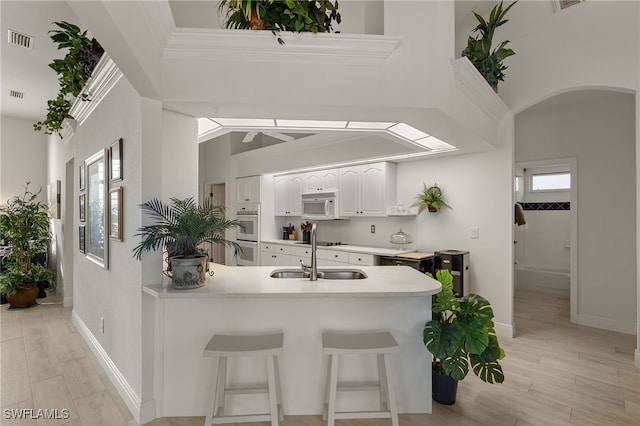 kitchen with kitchen peninsula, ornamental molding, a breakfast bar, sink, and white cabinetry