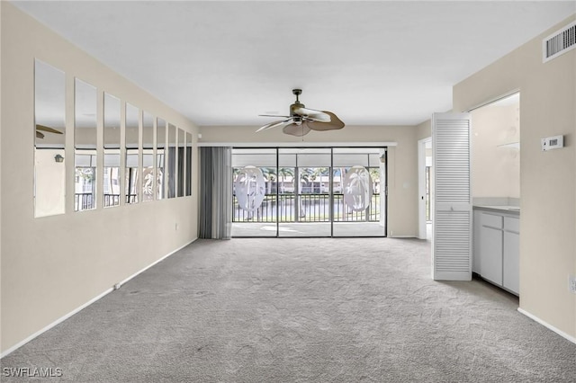 unfurnished living room with carpet floors, visible vents, baseboards, and a ceiling fan