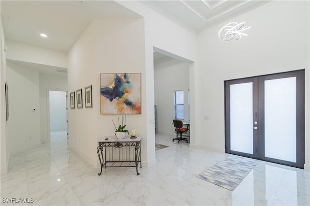 entrance foyer featuring a chandelier, a towering ceiling, and french doors