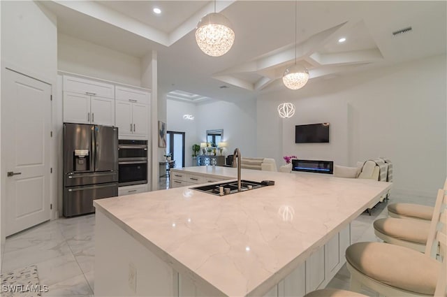 kitchen featuring stainless steel appliances, a kitchen island with sink, sink, decorative light fixtures, and white cabinetry