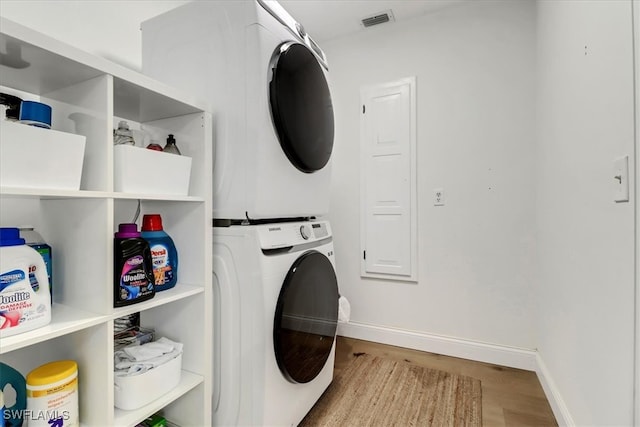 washroom featuring stacked washer and dryer, wood finished floors, laundry area, baseboards, and visible vents