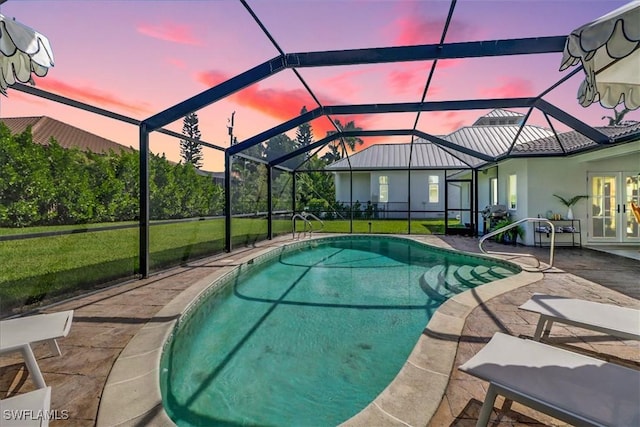 pool at dusk featuring a yard, french doors, a lanai, and a patio area