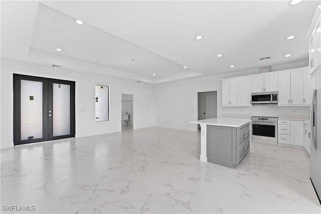 kitchen featuring a center island, a tray ceiling, stainless steel appliances, white cabinets, and french doors