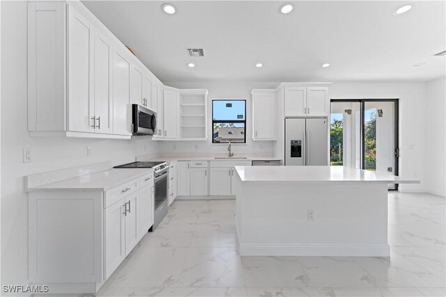 kitchen with appliances with stainless steel finishes, white cabinets, a kitchen island, and sink