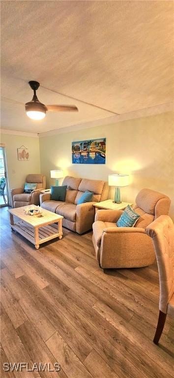 living room with hardwood / wood-style flooring, ceiling fan, crown molding, and a textured ceiling