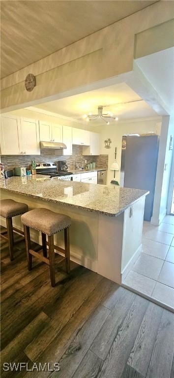 kitchen featuring a kitchen bar, white cabinetry, and light stone counters