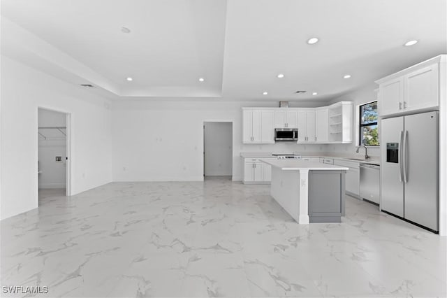 kitchen featuring a kitchen island, white cabinetry, stainless steel appliances, sink, and a tray ceiling