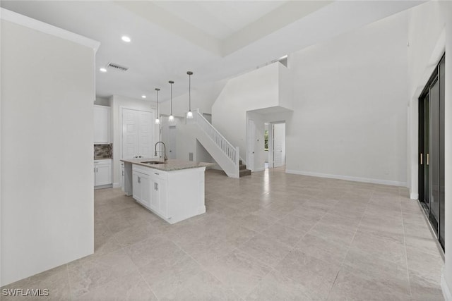 kitchen featuring pendant lighting, a center island with sink, white cabinets, sink, and light stone countertops