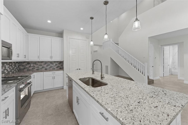 kitchen featuring light stone counters, stainless steel appliances, a kitchen island with sink, sink, and white cabinetry