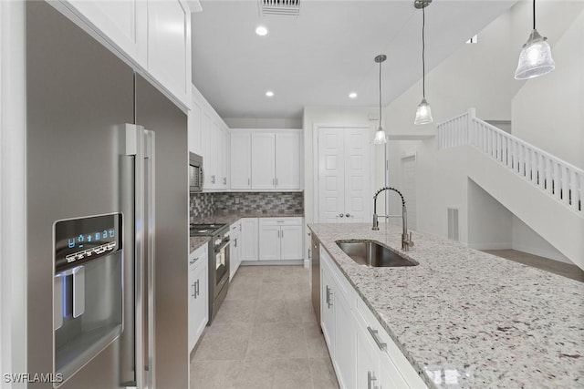 kitchen featuring light stone counters, sink, decorative light fixtures, high quality appliances, and white cabinetry