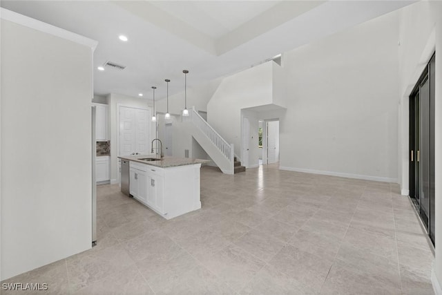 kitchen featuring stainless steel dishwasher, a kitchen island with sink, sink, decorative light fixtures, and white cabinetry