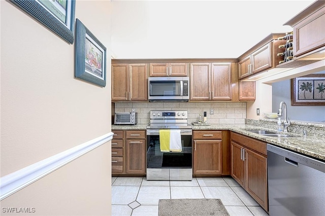 kitchen with sink, light tile patterned floors, appliances with stainless steel finishes, tasteful backsplash, and light stone counters