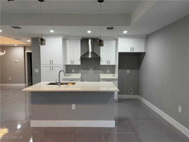 kitchen featuring wall chimney exhaust hood, an island with sink, pendant lighting, and sink