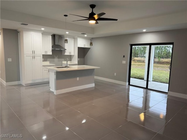 kitchen featuring white cabinets, wall chimney exhaust hood, sink, and a center island with sink