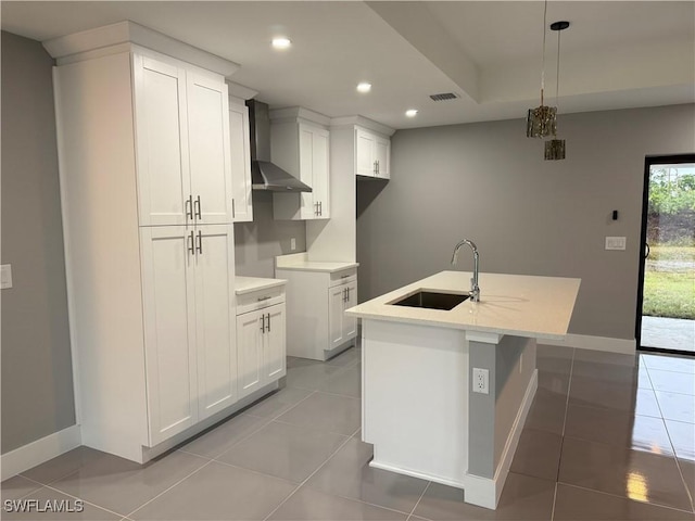 kitchen featuring white cabinets, a kitchen island with sink, wall chimney range hood, and pendant lighting