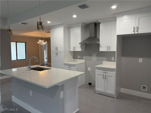 kitchen featuring decorative light fixtures, sink, wall chimney range hood, and white cabinetry